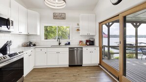 A modern kitchen with white cabinets, stainless steel appliances, and a wooden deck overlooking a body of water. - No steps, Game Room, Canoe & Kayaks, Dock, All Paved Roads! 10 min to 2 marinas! (Jasper)