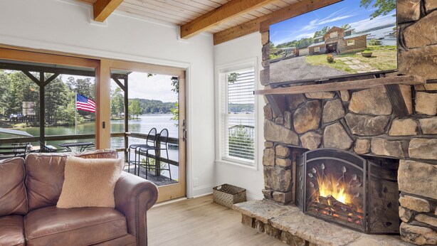 A cozy living room with a stone fireplace, leather sofa, and large windows overlooking a scenic lake. - No steps, Game Room, Canoe & Kayaks, Dock, All Paved Roads! 10 min to 2 marinas! (Jasper)