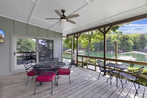 Relax on the deck with a view of the water, surrounded by lush greenery and a dock in the distance.