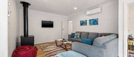 Una sala de estar moderna con un sofá gris, un sillón inflable rojo, una chimenea negra, un televisor de pantalla plana y dos obras de arte abstractas en la pared.