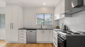 A modern kitchen with white cabinetry, a stainless steel dishwasher, a gas stove, and a window with blinds. - Alpine View Cottage - Close to town (Bright)