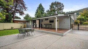 A single-story house with a covered patio, a barbecue grill, and a TV mounted on the wall. - Alpine View Cottage - Close to town (Bright)