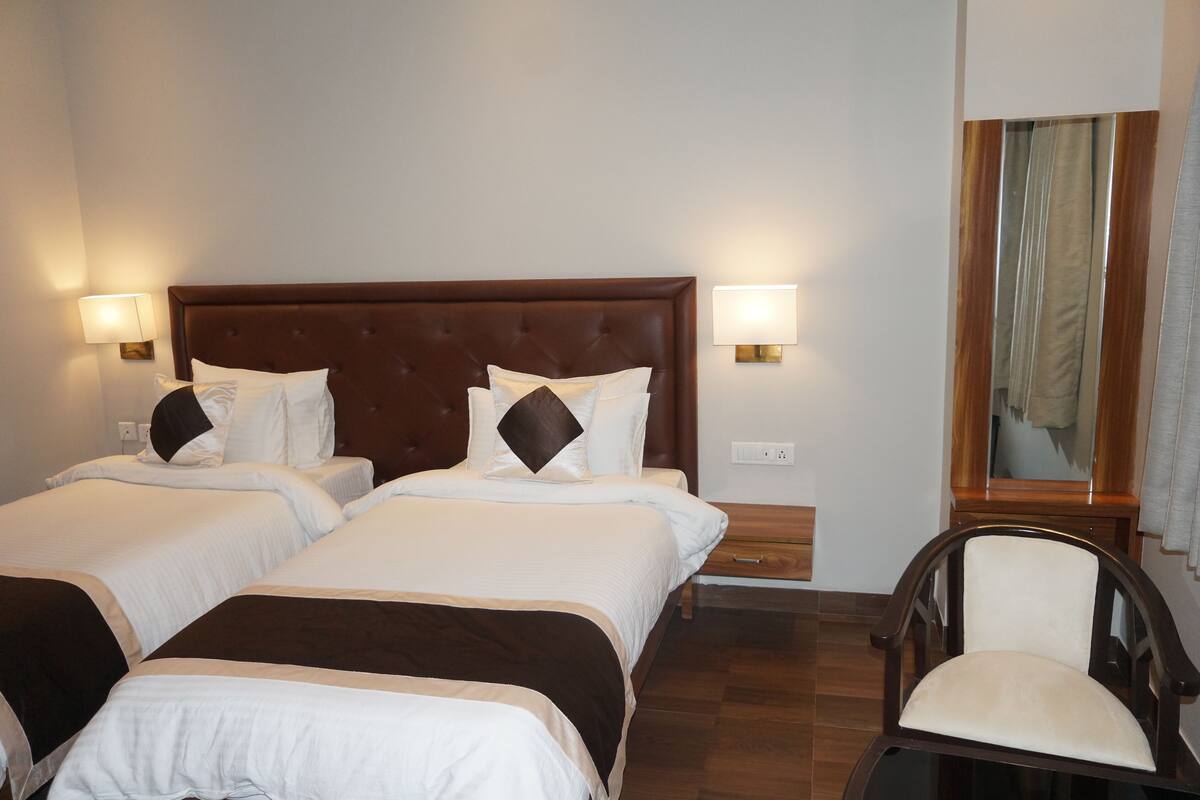 Habitación de hotel con dos camas, cabecero de madera, lámparas de noche, una silla y un espejo.