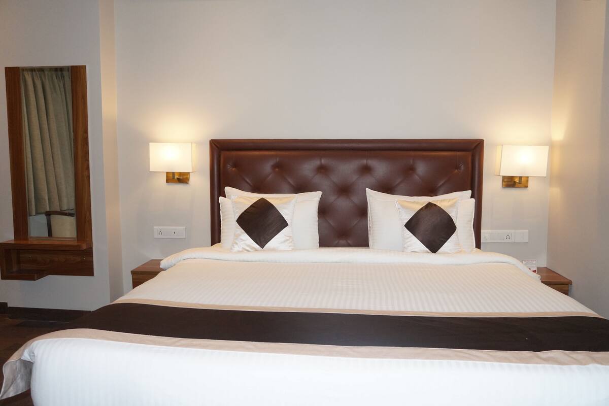 Una habitación de hotel con una cama grande, dos lámparas de noche, un cabecero de madera y un ventanal con cortinas.