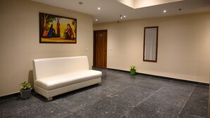 Una hall con un divano bianco, un quadro appeso al muro, una porta e una pianta in vaso.