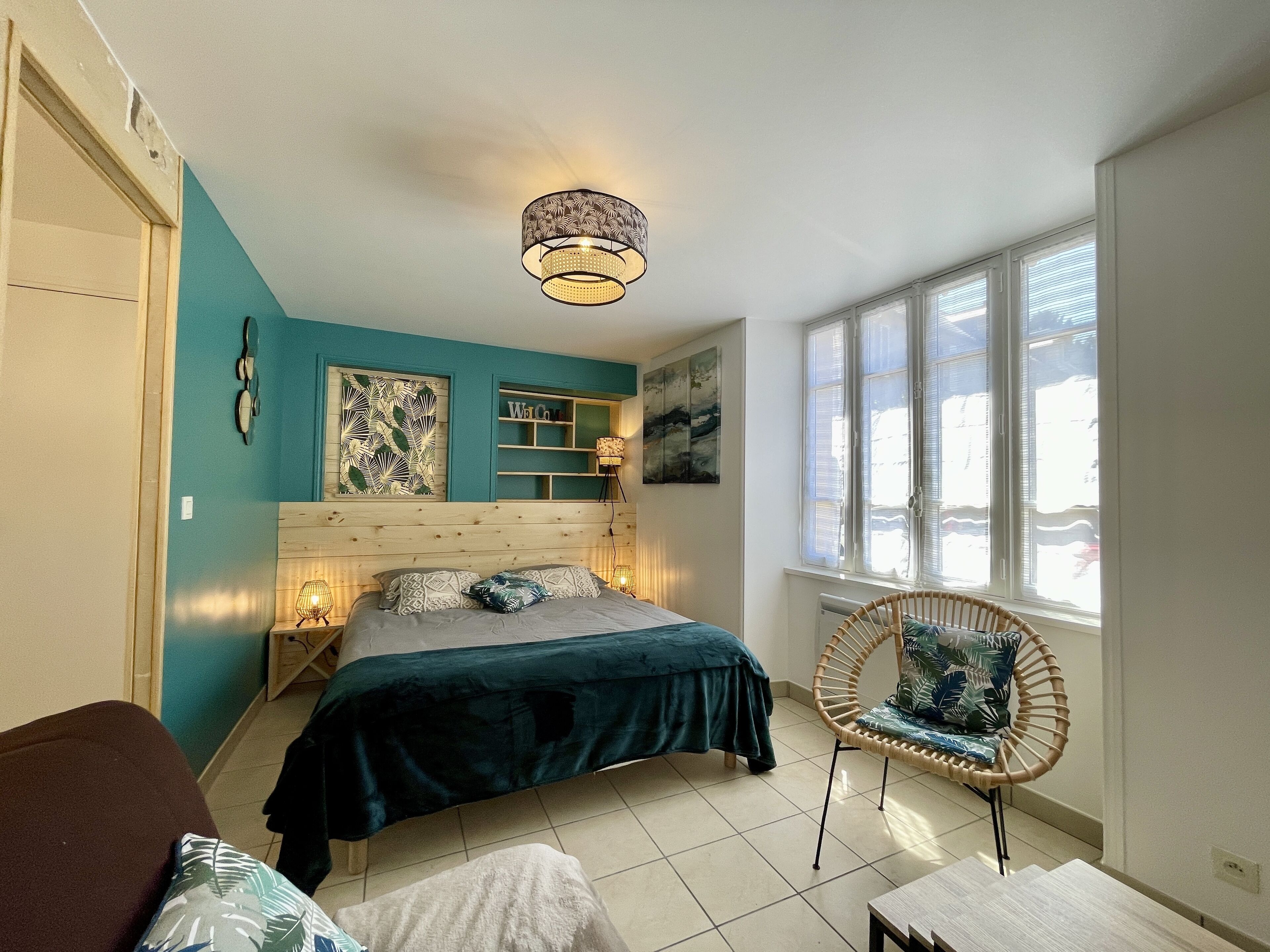 A bedroom with a bed, a chair, a window, and artwork on the wall.
