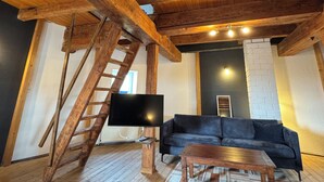 A rustic interior with exposed wooden beams, a black leather sofa, a wooden coffee table, and a mounted flat-screen TV.