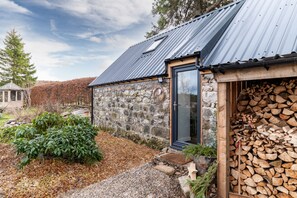 Una casa in pietra con tetto in metallo, una porta di legno e una pila di legna da ardere all'esterno.