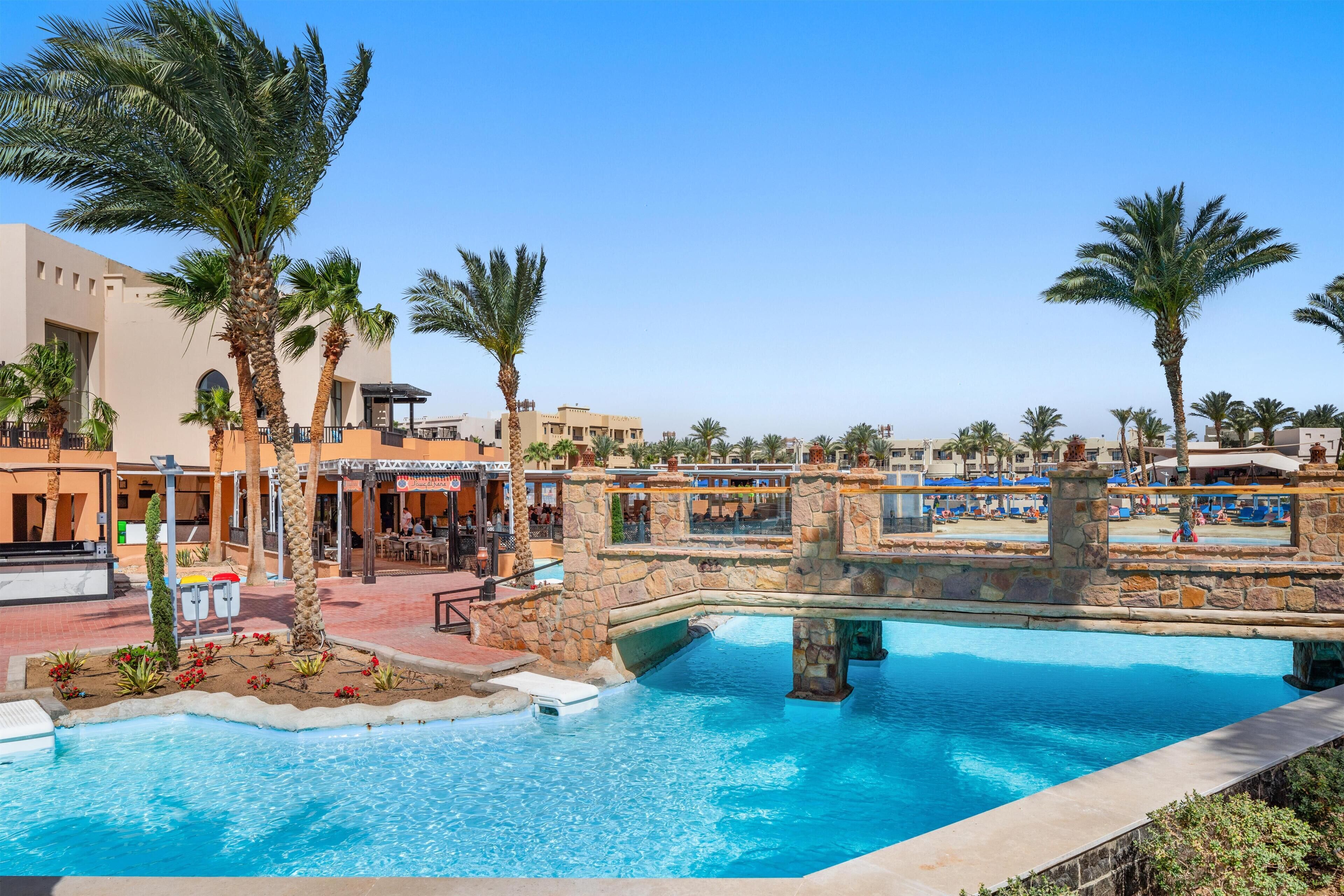 A pool area with palm trees, a stone bridge, and a bar area.