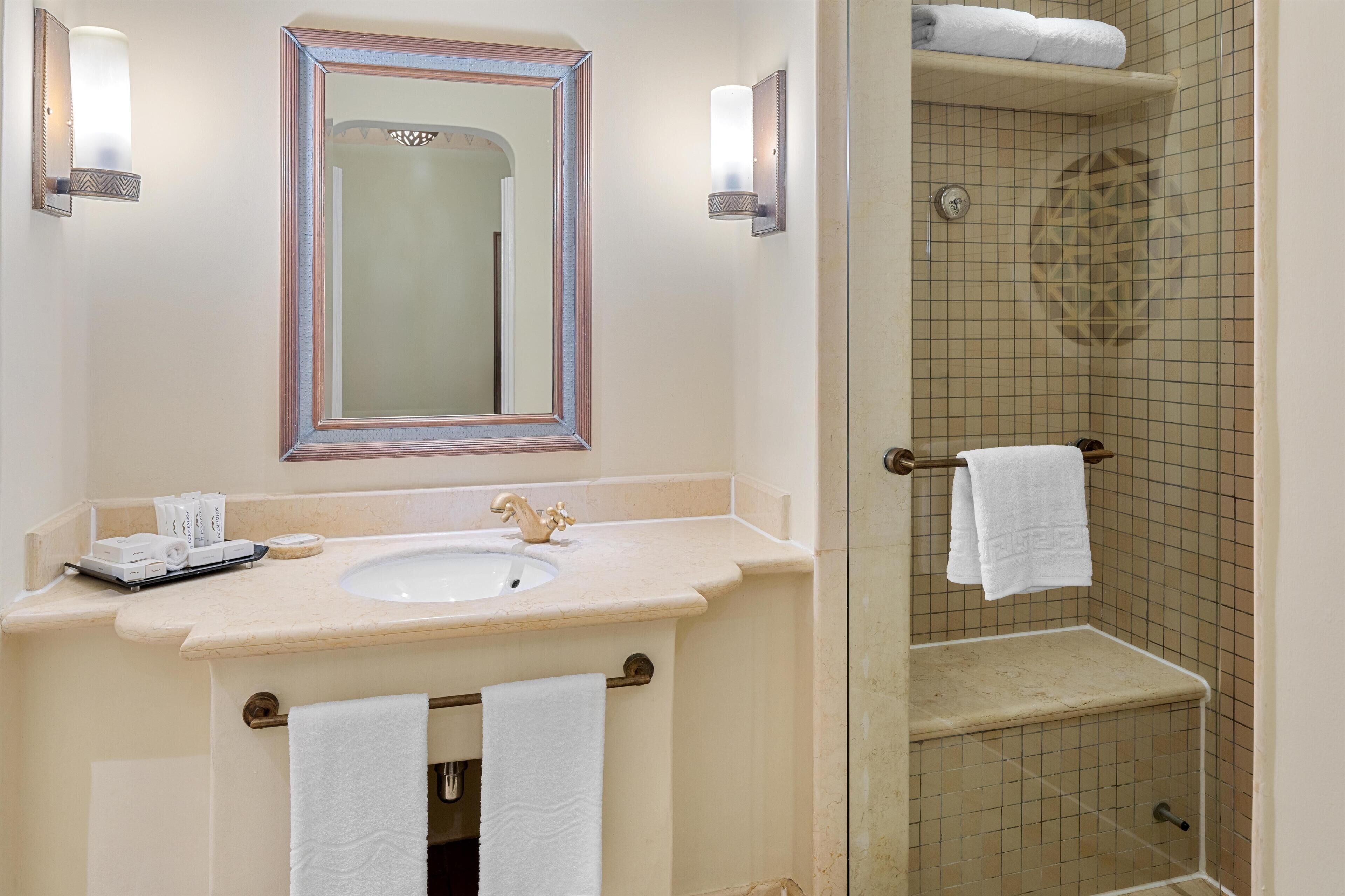 A bathroom with a sink, mirror, towel rack, and shower area.