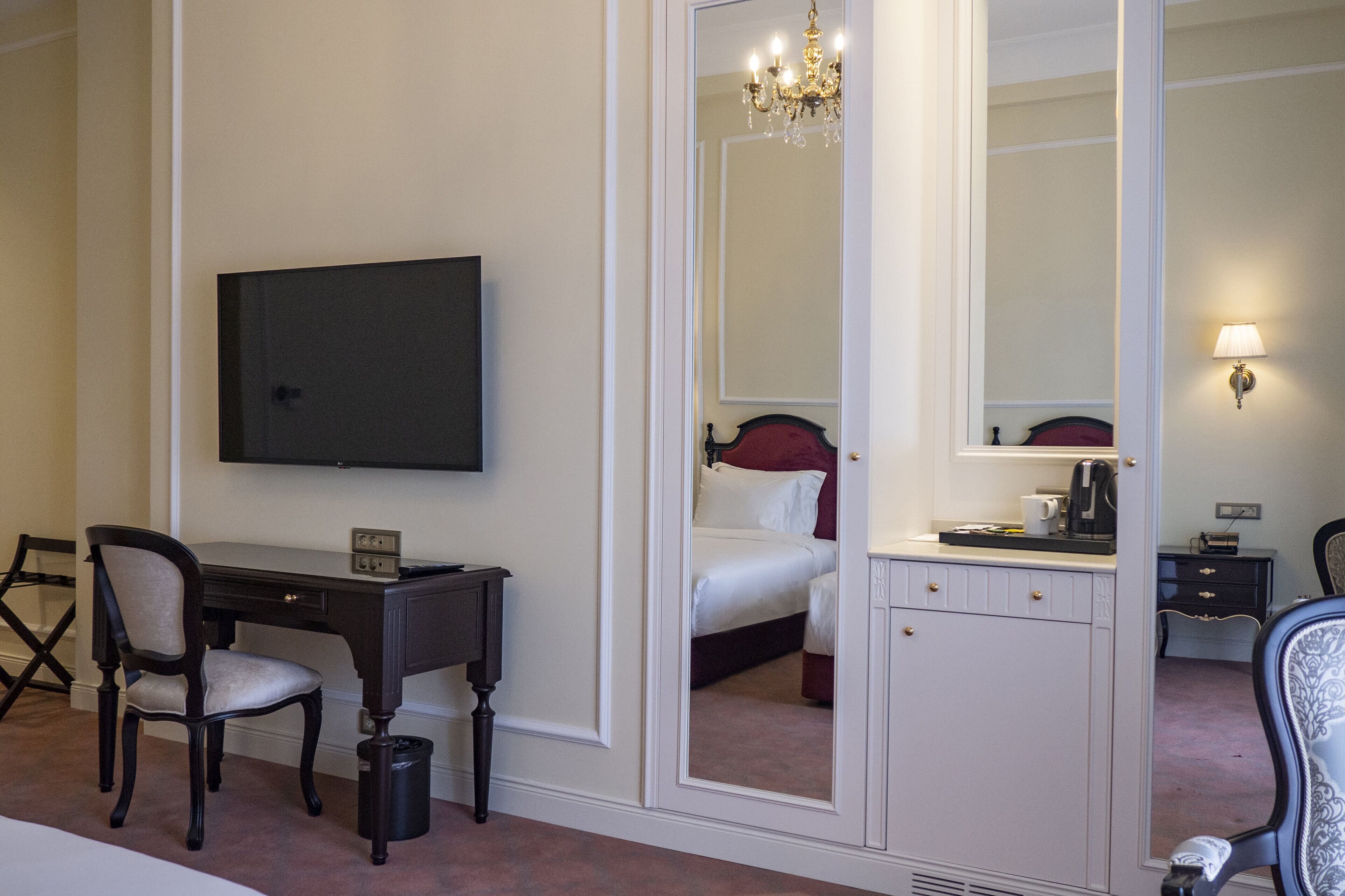 Une chambre d’hôtel équipée d’un lit, d’un bureau, d’une chaise, d’une télévision, d’un miroir et d’un lustre.