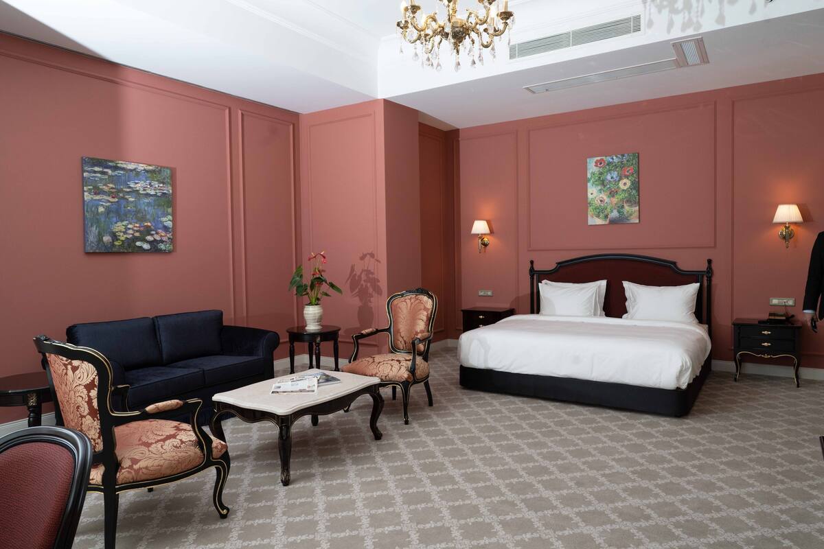 Habitación de hotel con cama, sofá, dos sillones, una mesa de centro y dos cuadros en las paredes.