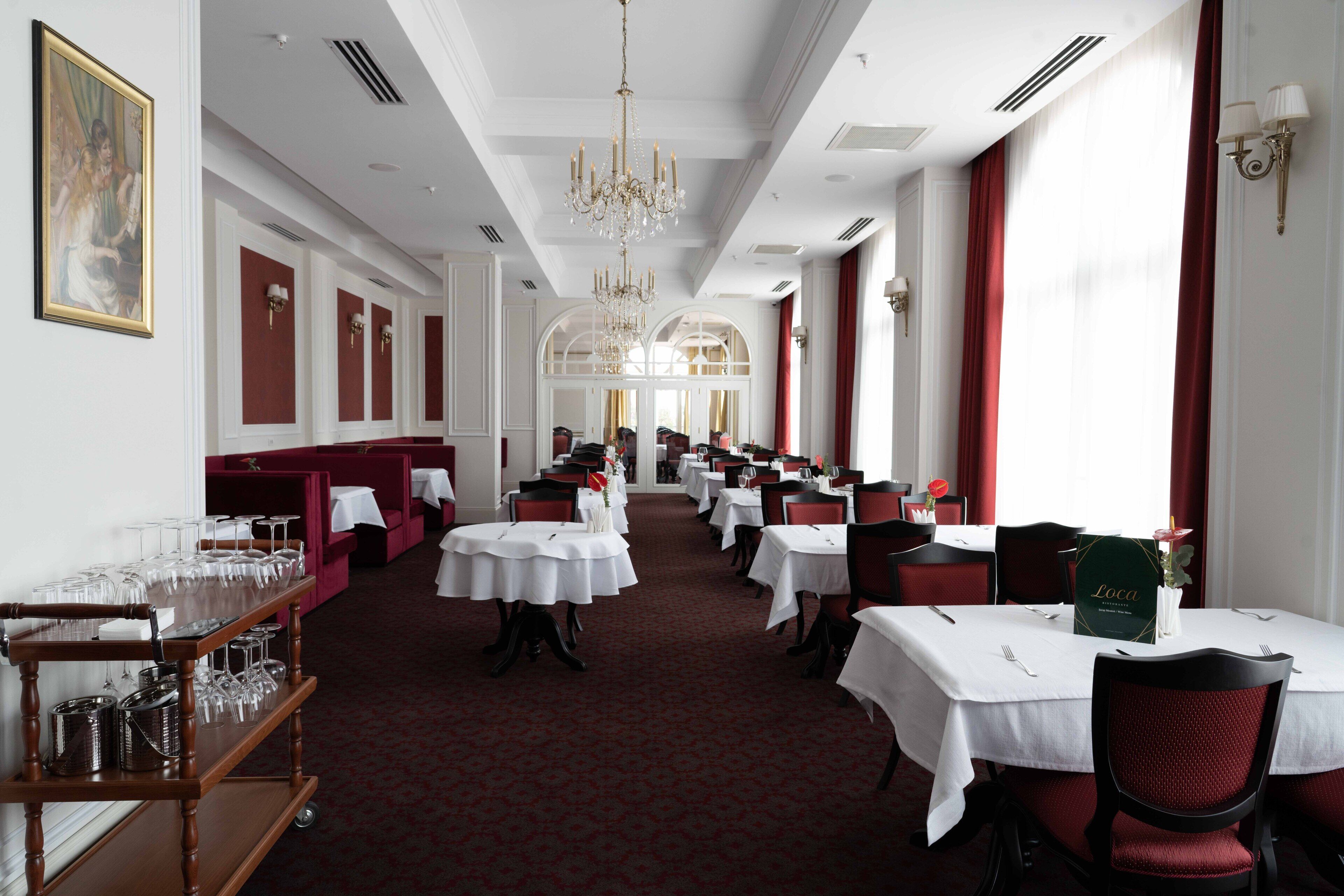 A formal dining area with multiple tables and chairs, a chandelier, and a red carpeted floor.