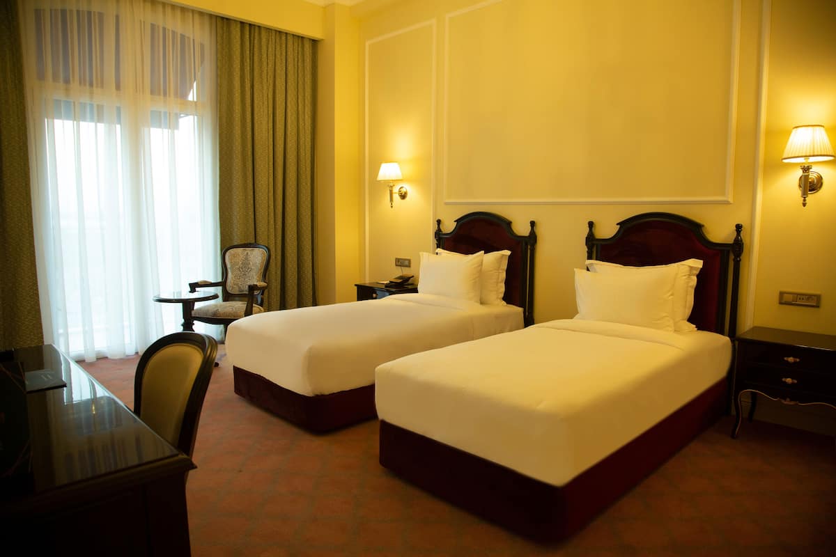 Habitación de hotel con dos camas, un escritorio, una silla y una ventana con cortinas.
