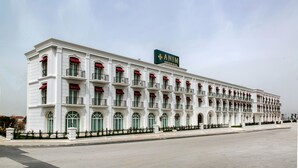 Un edificio grande y blanco con un letrero que dice "ANIM" y un logotipo verde. Tiene varios balcones con toldos rojos y ventanas verdes.