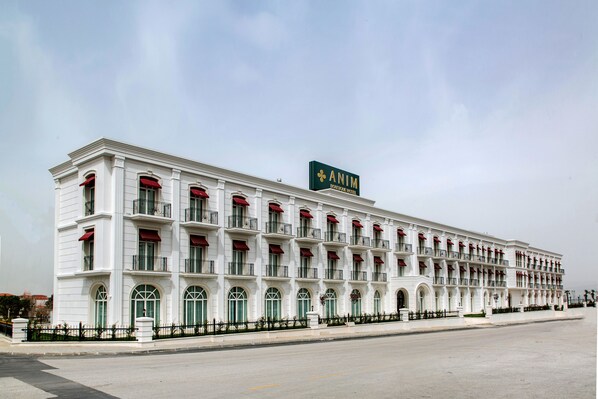 A large, white building with a sign reading "ANIM" and a green logo. It has multiple balconies with red awnings and green windows. - ANIM Boutique Hotel (Denizli)