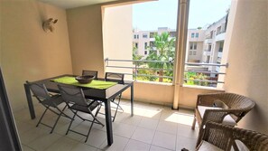 Un balcon avec une table à manger, des chaises et un fauteuil en osier.