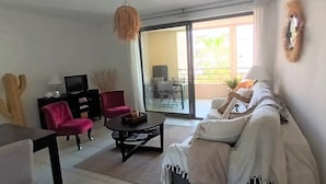 A living room with a sofa, two chairs, a coffee table, a TV, and a sliding glass door leading to an outdoor area with a table and chairs. - "Le Côté port" Type 3 near the port - wifi - air conditioning - parking (LA CIOTAT)