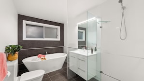 Een moderne badkamer met een vrijstaand bad, een douchecabine met glazen wanden en een wastafelmeubel met spiegel.