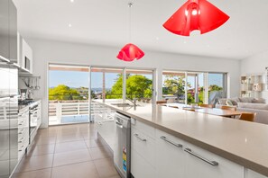 A modern kitchen with a large island, sliding glass doors leading to a balcony, and a red pendant light.