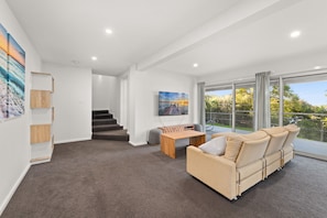 A modern living room with a sofa, a coffee table, and a painting on the wall. There is a staircase leading to another level.