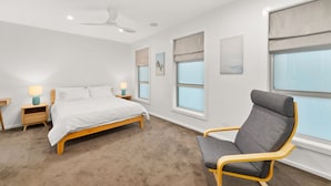 Een slaapkamer met een bed, nachtkastjes, een stoel, een plafondventilator en ramen met jaloezieën.