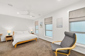 Quarto com cama, mesas de cabeceira, uma cadeira, ventilador de teto e janelas com persianas.
