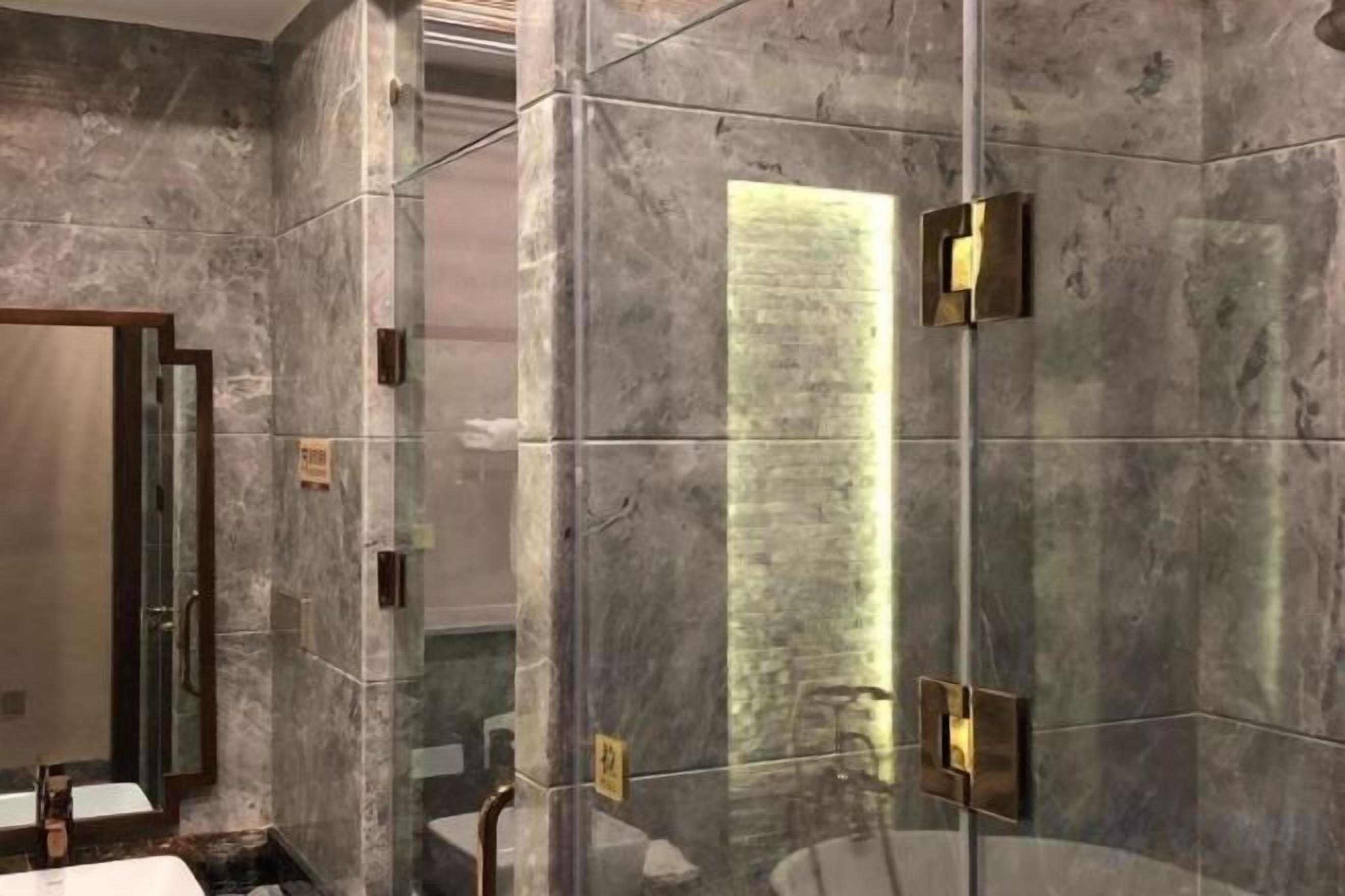 A bathroom with a glass shower enclosure, a marble wall, and a mirror.