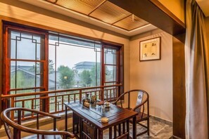 A room with a traditional wooden table and chairs, large windows with a view of buildings, and a framed picture on the wall. - Laozi Boxue International Hotel (Luyi)