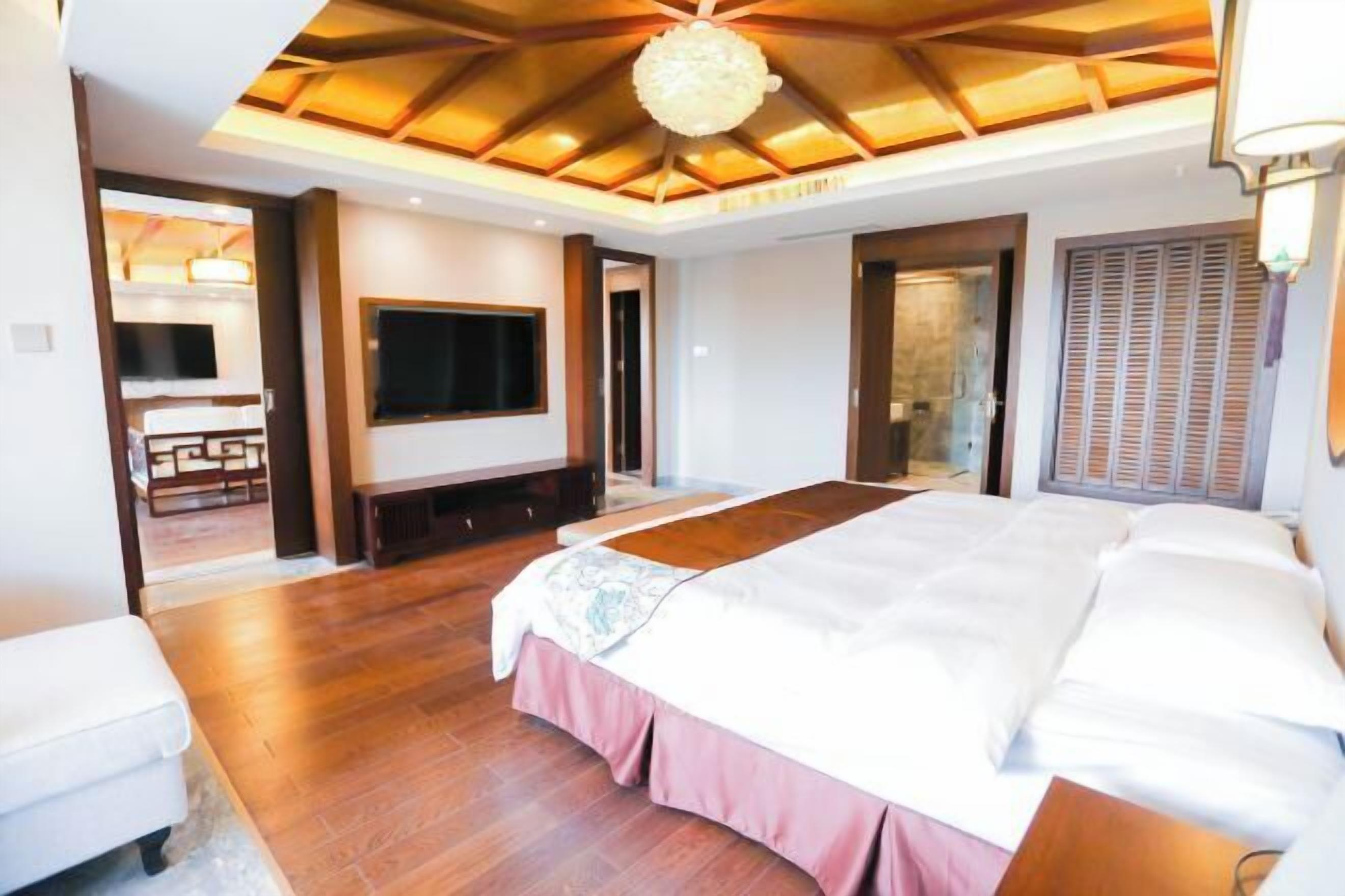 A bedroom with a large bed, a TV, and a wooden ceiling.