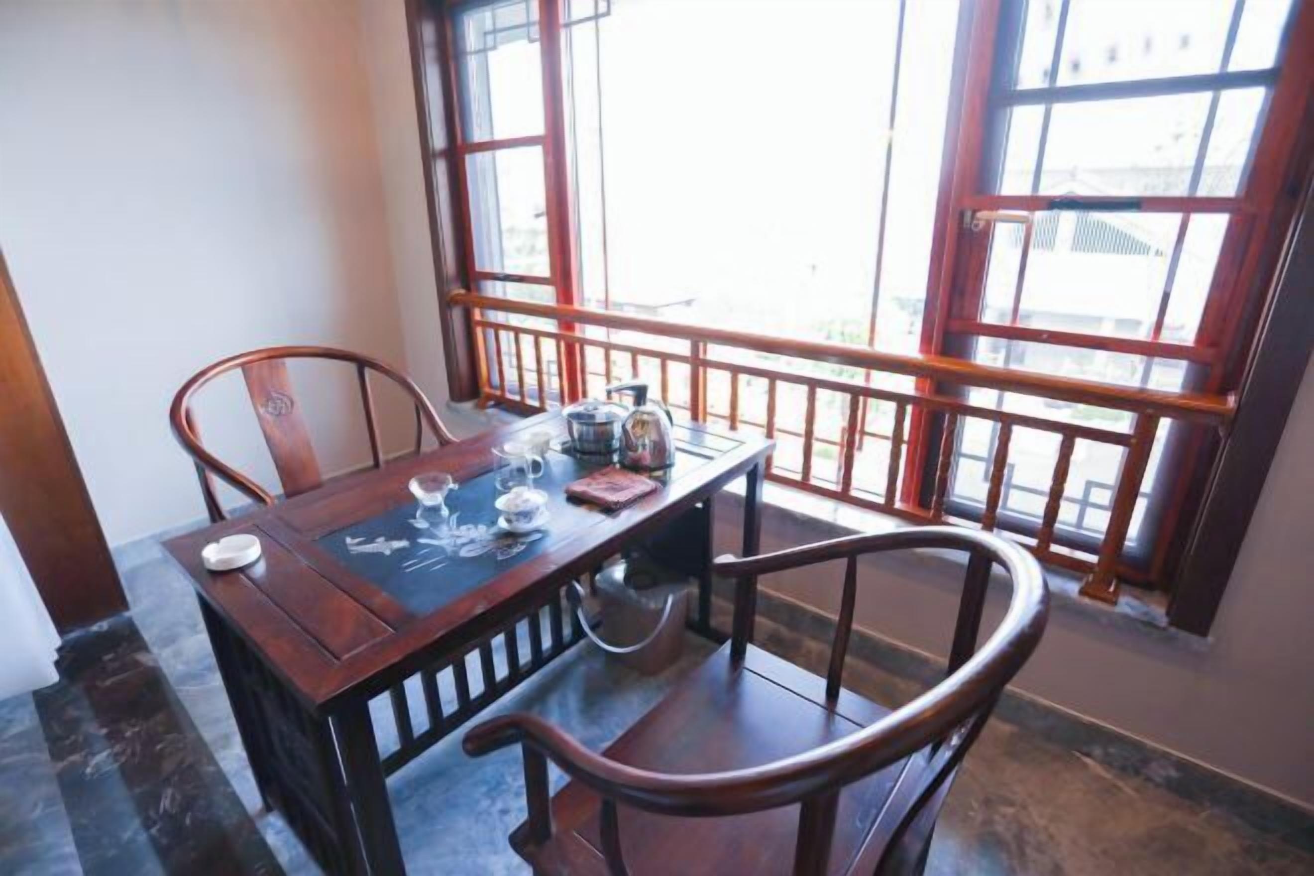 A dining area with a wooden table and chairs, a window with a view, and a small table with a teapot and cups.