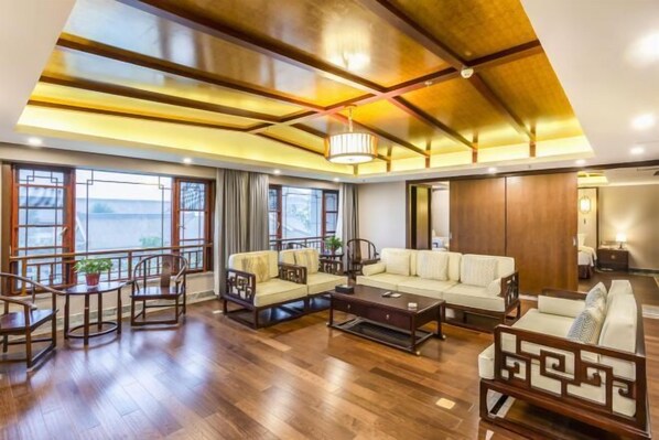 A spacious living room with wooden flooring, a large sofa, a coffee table, and a dining area with chairs. - Laozi Boxue International Hotel (Luyi)