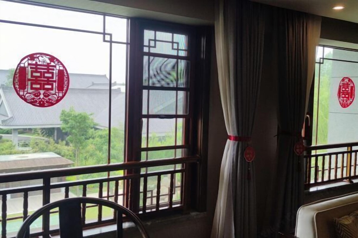 A room with a balcony, a window with a view, and a red decorative element on the window.