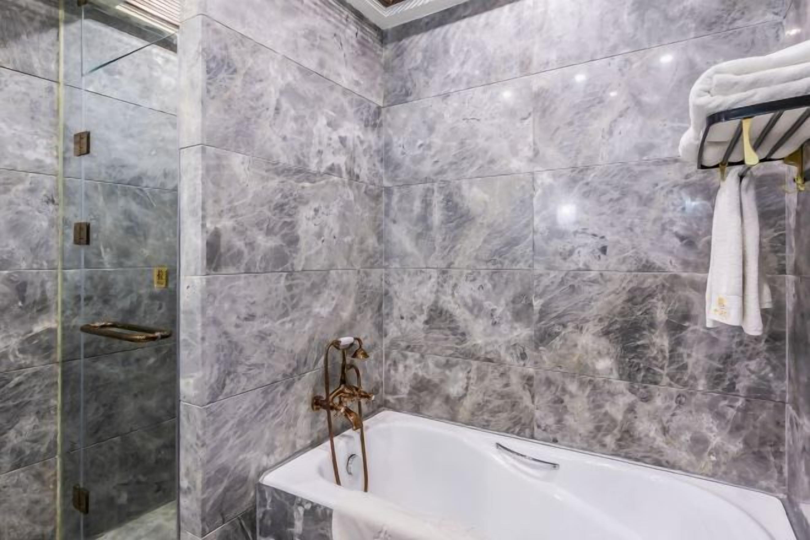 A bathroom with a freestanding bathtub, marble walls, and a towel rack.