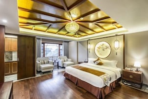 A hotel room with a large bed, a desk, a chair, a small table, and a window.
