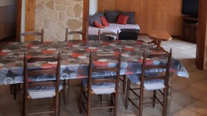 Un espace repas avec une grande table et des chaises, un mur en pierre, un banc en bois et un téléviseur en arrière-plan.