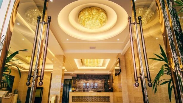 Een hotellobby met een centraal gelegen receptiebalie, een ronde kroonluchter en hoge zuilen.