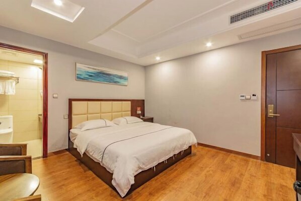 A hotel room with a bed, a wooden floor, a painting on the wall, and a door.