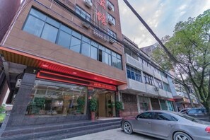 A multi-story building with a prominent entrance, large windows, and a visible car parked in front. - Fudu Hotel (Wuxue)