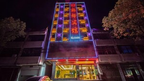 Een hotel met een opvallend verticaal bord waarop Chinese karakters staan, een goed verlichte ingang en een auto ervoor geparkeerd.