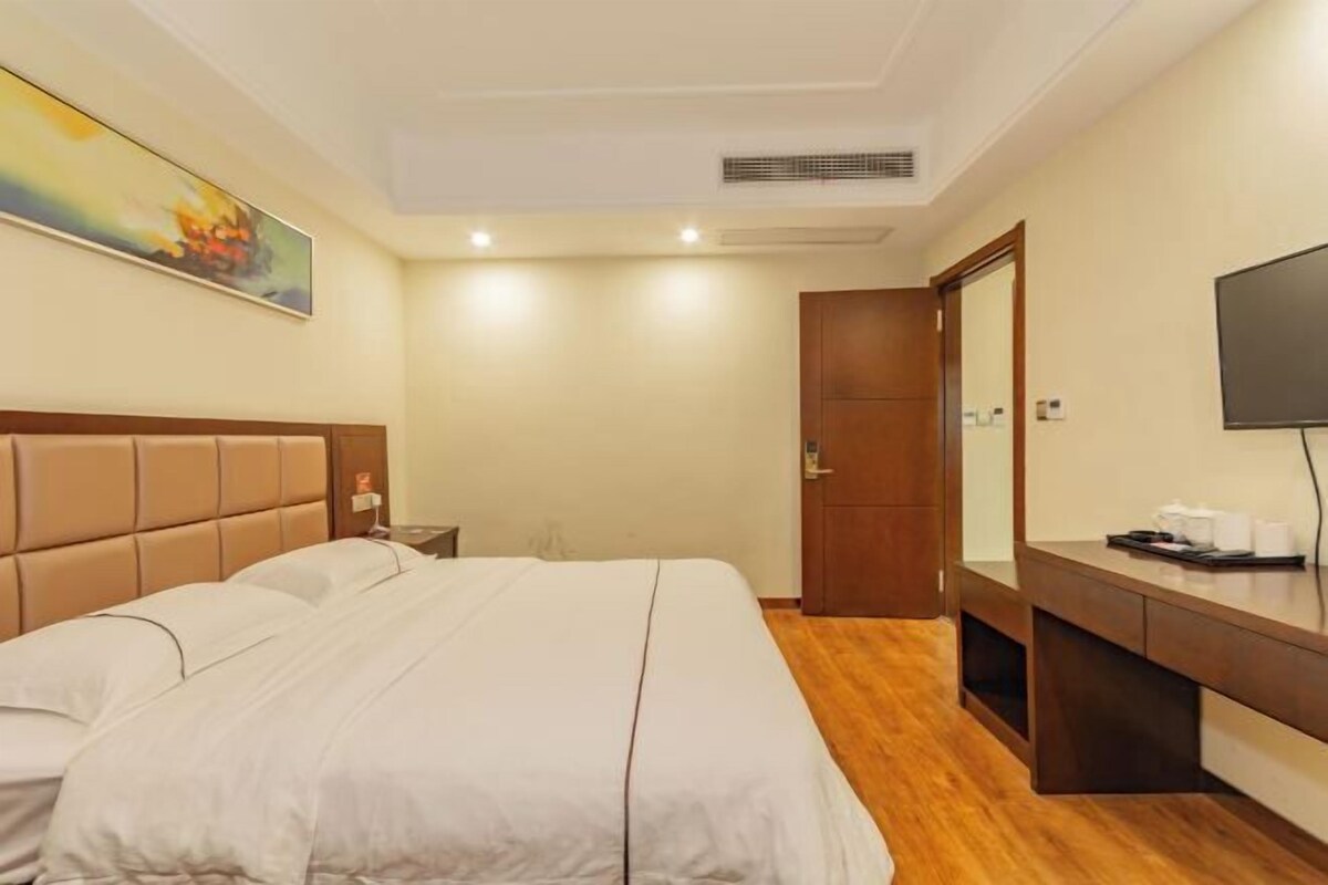 Quarto de hotel com uma cama grande, uma escrivaninha de madeira, uma televisão e uma porta que dá para outro espaço.