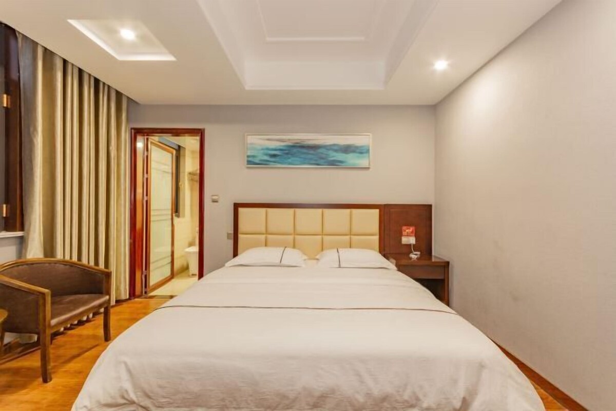 Quarto de hotel com uma cama grande, uma mesinha de cabeceira, uma cadeira e um quadro na parede.