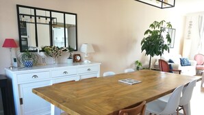 Un comedor con una mesa de madera y sillas blancas, un aparador blanco con objetos decorativos, y un espejo grande sobre el aparador.