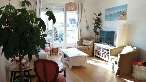 Una sala de estar bien iluminada, con un ventanal grande, un televisor y una zona de estar confortable.