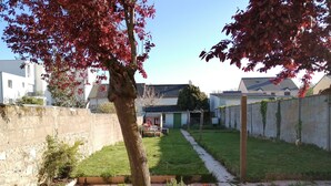 Un patio trasero residencial con un camino pavimentado, un árbol de hojas rojas y una pequeña zona de jardín.