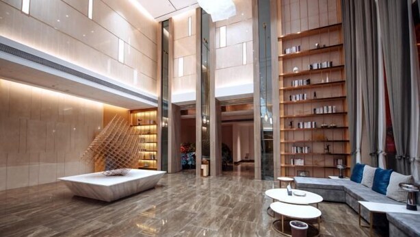 Um hall amplo com design moderno, destacando uma área de estar central com sofás e mesas, uma escadaria e uma grande estante de livros.