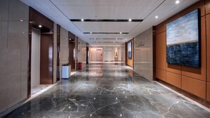 Um corredor moderno de hotel com piso de mármore, painéis de madeira e uma grande pintura abstrata na parede.