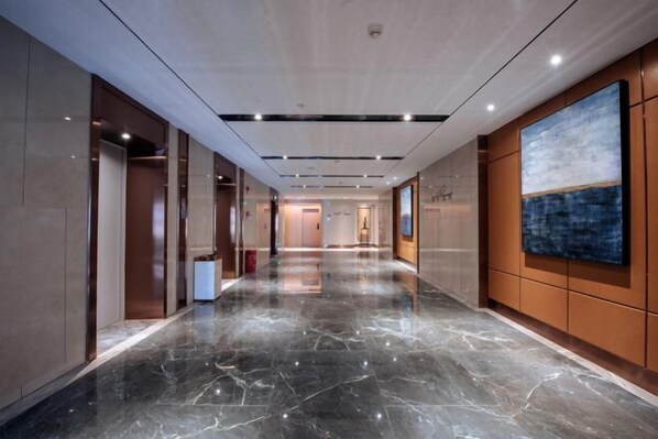 Een moderne hotelgang met marmeren vloer, houten lambrisering en een groot abstract schilderij aan de wand.