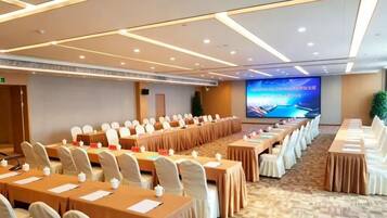 A conference room with long tables, chairs, and a large screen.