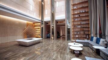 A spacious lobby with a marble floor, a central seating area, and a large bookshelf.